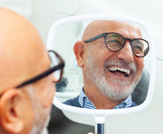 A senior man admiring his smile in a hand mirror