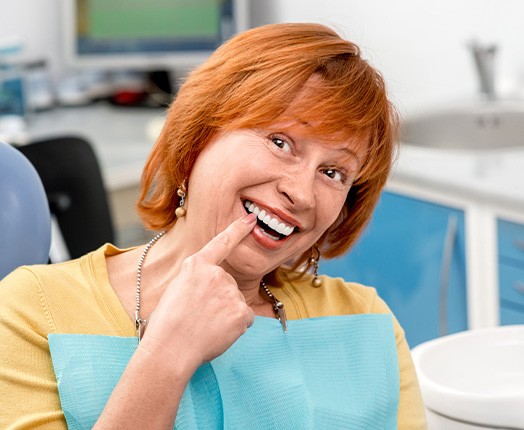 A smiling woman pointing out her new dental implant