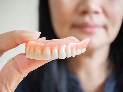 A blurred woman holding an upper denture between her fingers