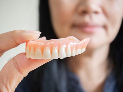 A blurred dental hygienist holding a removable denture