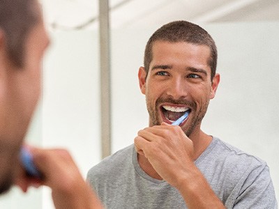 A young man brushing his teeth in front of a bathroom mirror