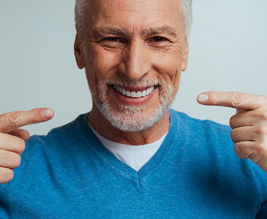 An older smiling man pointing to his new dentures