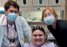 Two dental team members wearing protective gear with dental patient