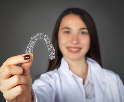 Smiling woman holding an Invisalign clear braces tray