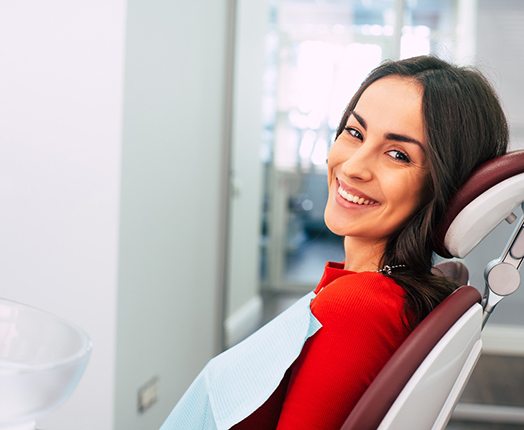 A smiling woman sitting in a dental chair and wearing a red sweater
