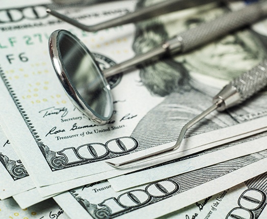 Some dental tools laying on top of hundred-dollar bills