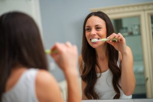 Woman brushing her teeth and looking at her reflection.
