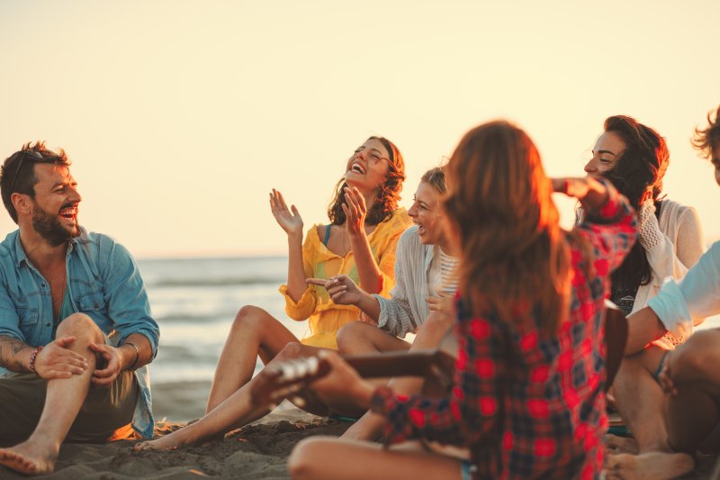 Happy friends sitting on a beach and laughing