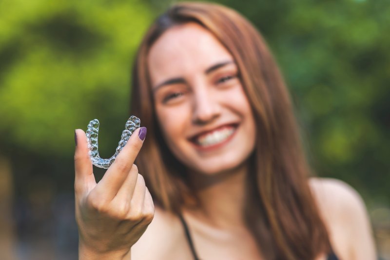 A smiling woman holding an Invisalign tray