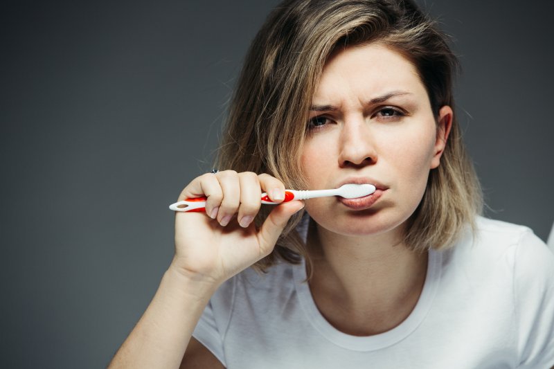 A frowning woman brushing her teeth