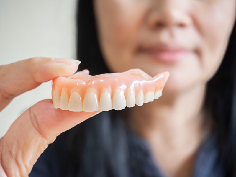 A denture that looks white and bright held between two fingers