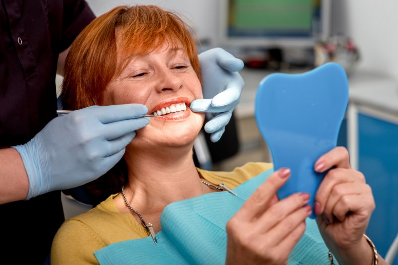 An older woman admiring her new dentures with a hand mirror