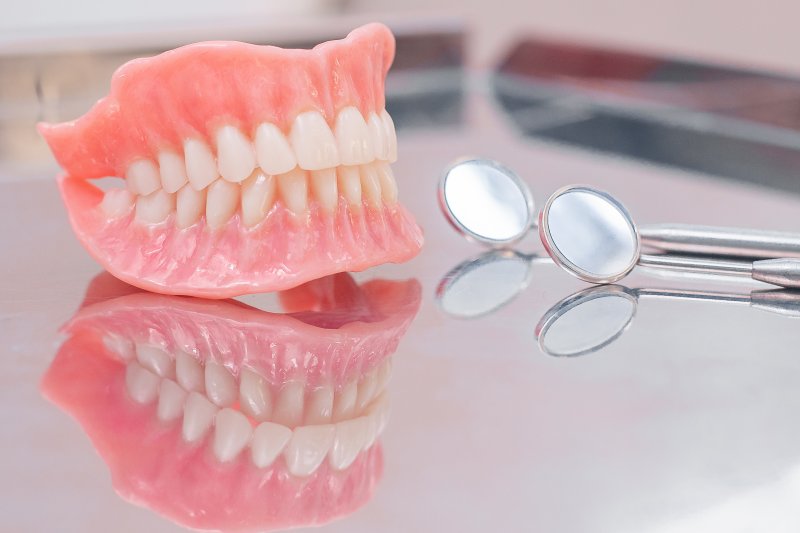 A pair of full dentures next to dental tools